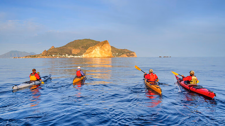 A group of people kayaking in the sea with a small green island behind