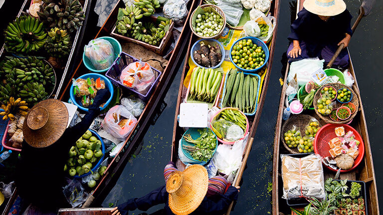 Aerial view of several boats filled with fresh produce at a traditional floating market. luxury food and wine trips.