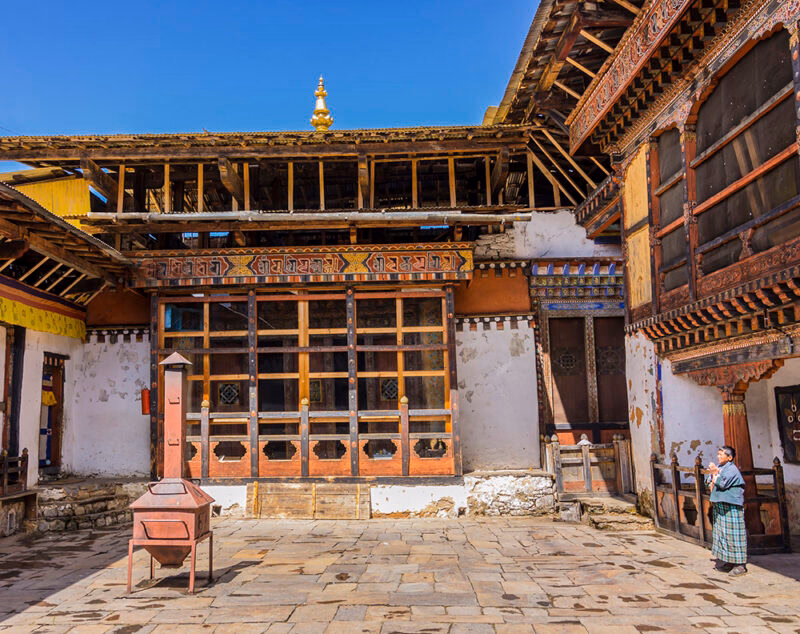 A person stands in a stone courtyard before a large traditional building with ornate wooden window frames.