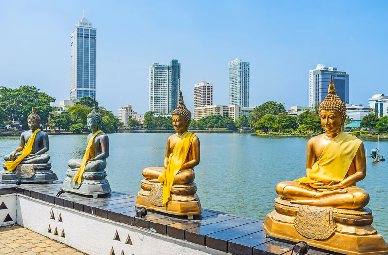 Golden Buddha statues by a lake with city skyscrapers, perfect for luxury Indian Subcontinent vacations.