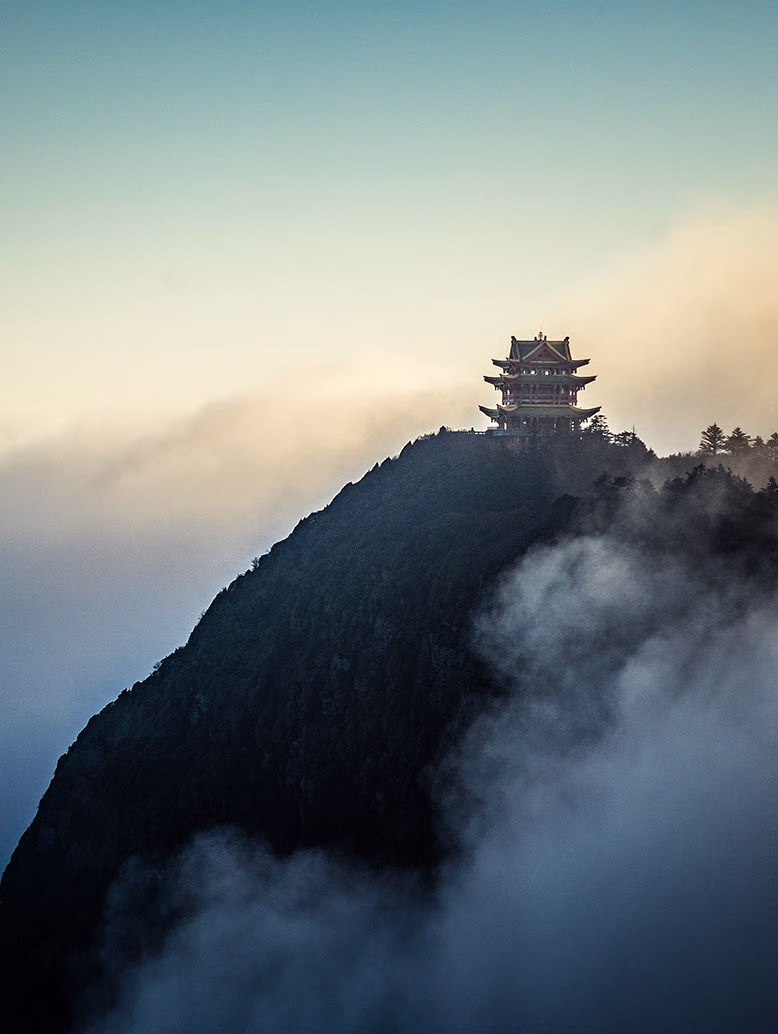 A gold-topped temple on a dark mountain peak above thick white clouds for luxury culture tours.