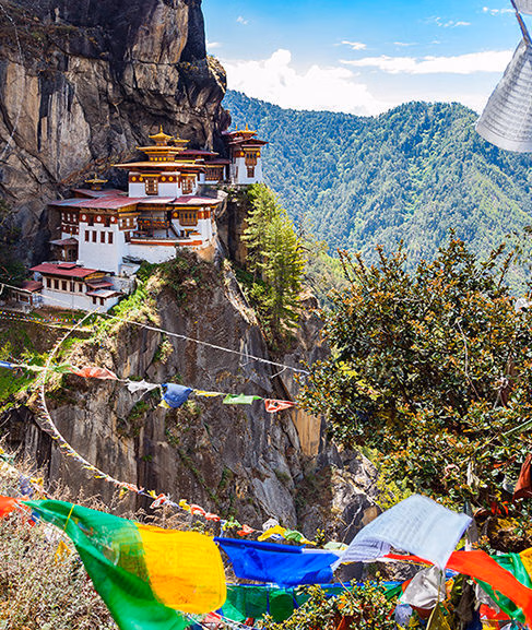 Tiger's Nest Monastery perched on a cliffside with prayer flags in the foreground for luxury asian family tours.