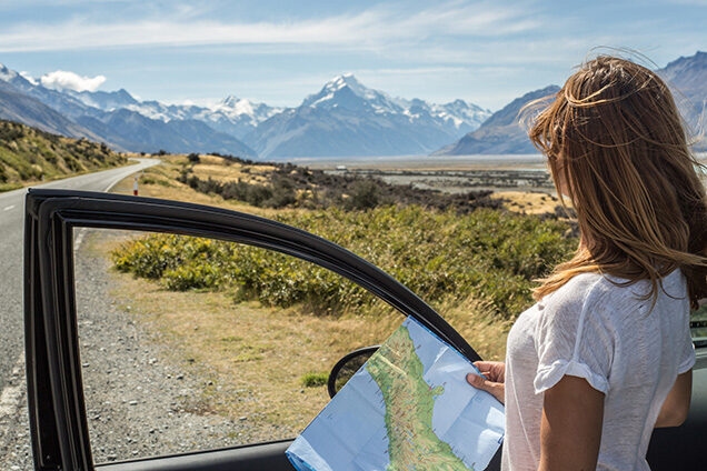 Woman holding a map next to a car overlooking mountains during luxury epic expeditions.