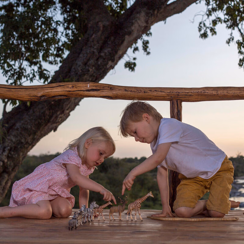 A young boy and girl playing with toy giraffes and zebras on a balcony during luxury African family safari vacations.