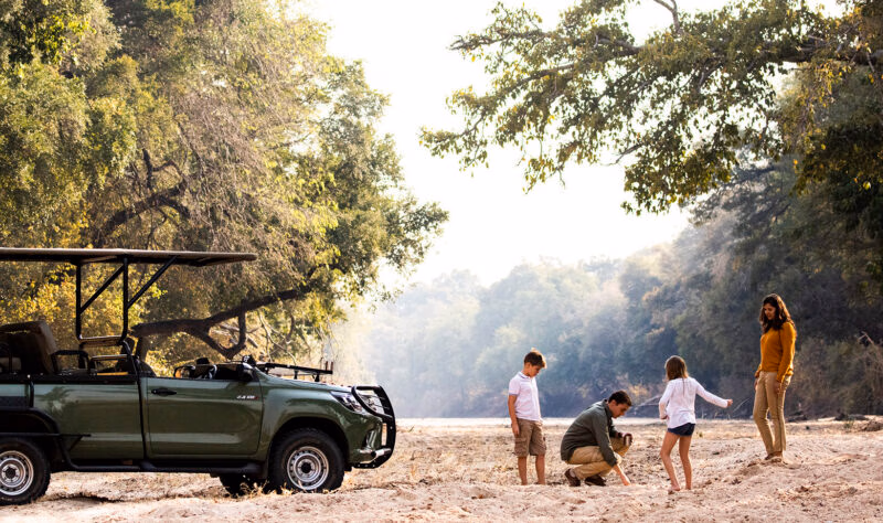 A family of four standing near a green off-road vehicle in a dry riverbed on luxury African family safari trips.