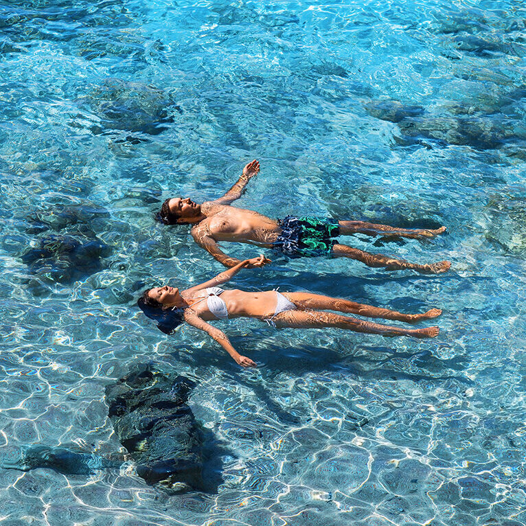 A couple floating on their backs in clear blue ocean water during luxury trips for two.