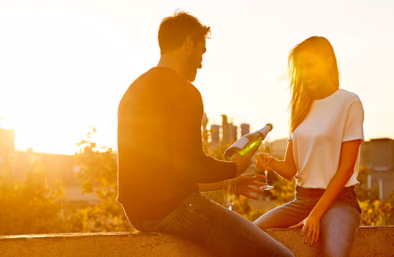 Man pouring champagne for a woman at sunset on a rooftop during luxury Honeymoons.