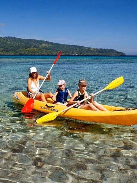 People in a yellow kayak on crystal clear ocean water with hills in the background on luxury Family vacations.