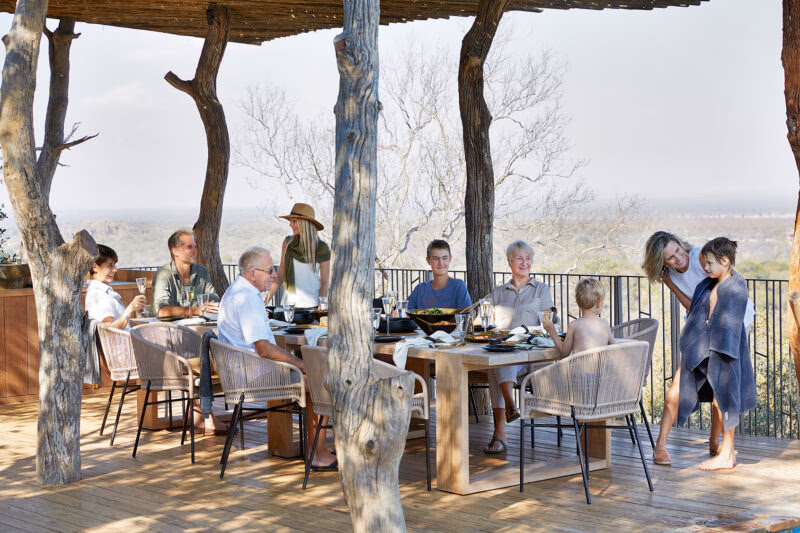 Family members sitting at a long wooden table on an outdoor deck during luxury Family vacations.