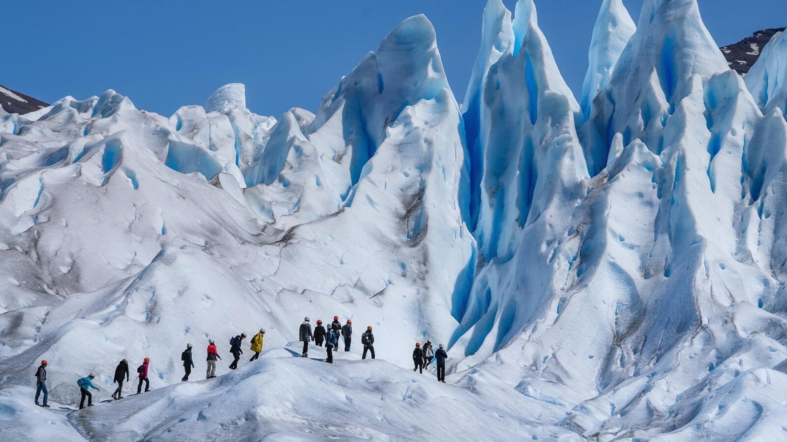Hikers walk across a jagged blue glacier on one of their epic expeditions.