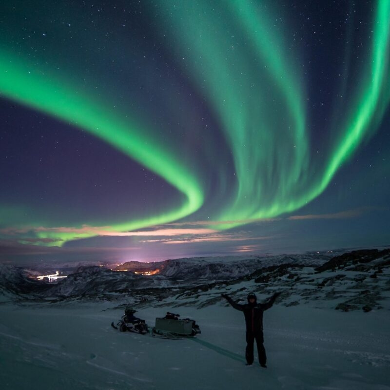 A person celebrating under the green Northern Lights during luxury Europe family trips.