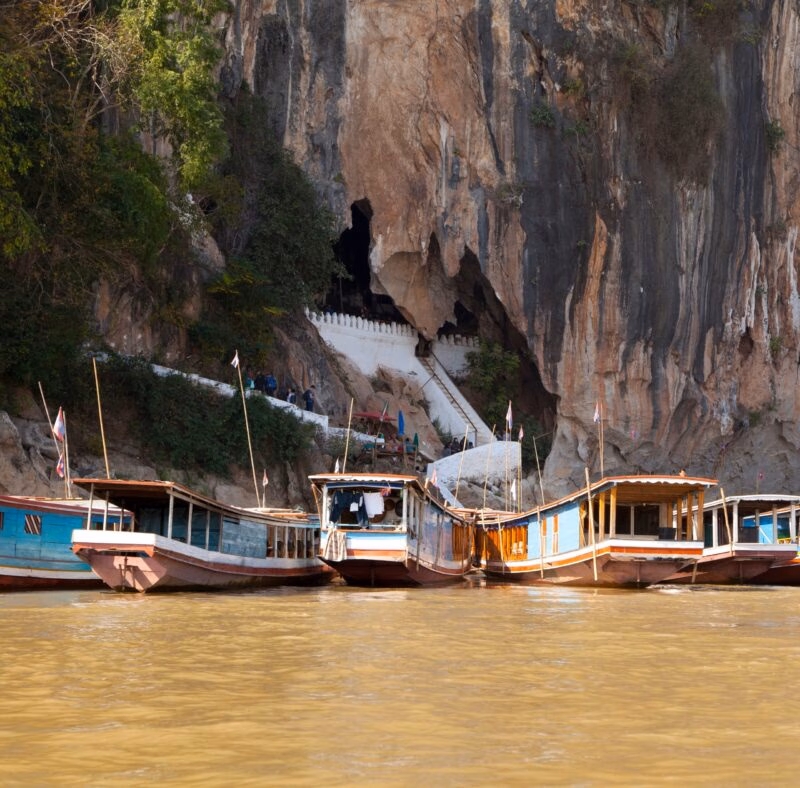 Longtail boats moored at the base of limestone cliffs near Pak Ou Caves, part of luxury Laos holidays.