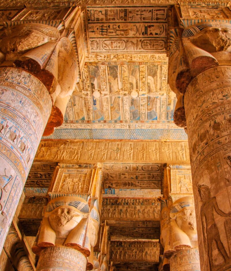 Massive, painted temple columns with carved figures and hieroglyphs supporting a richly decorated ceiling. Experience this on luxury Middle East trips.