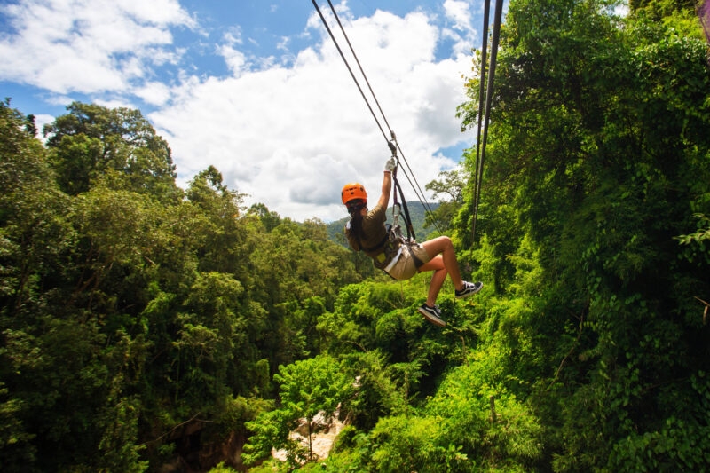 A person ziplining over a lush green jungle canopy during luxury asian family tours.
