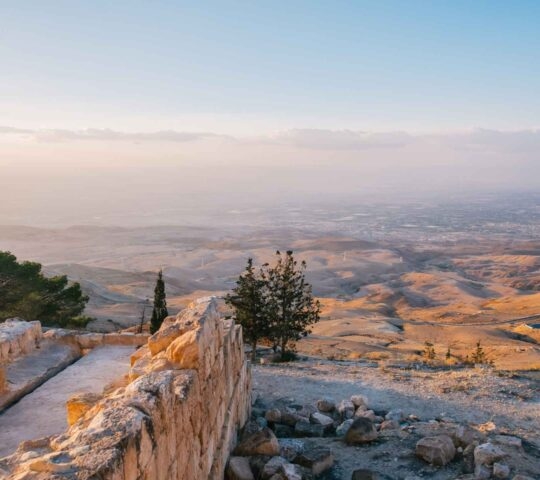 A panoramic view of a hazy desert valley seen from an ancient stone wall viewpoint.