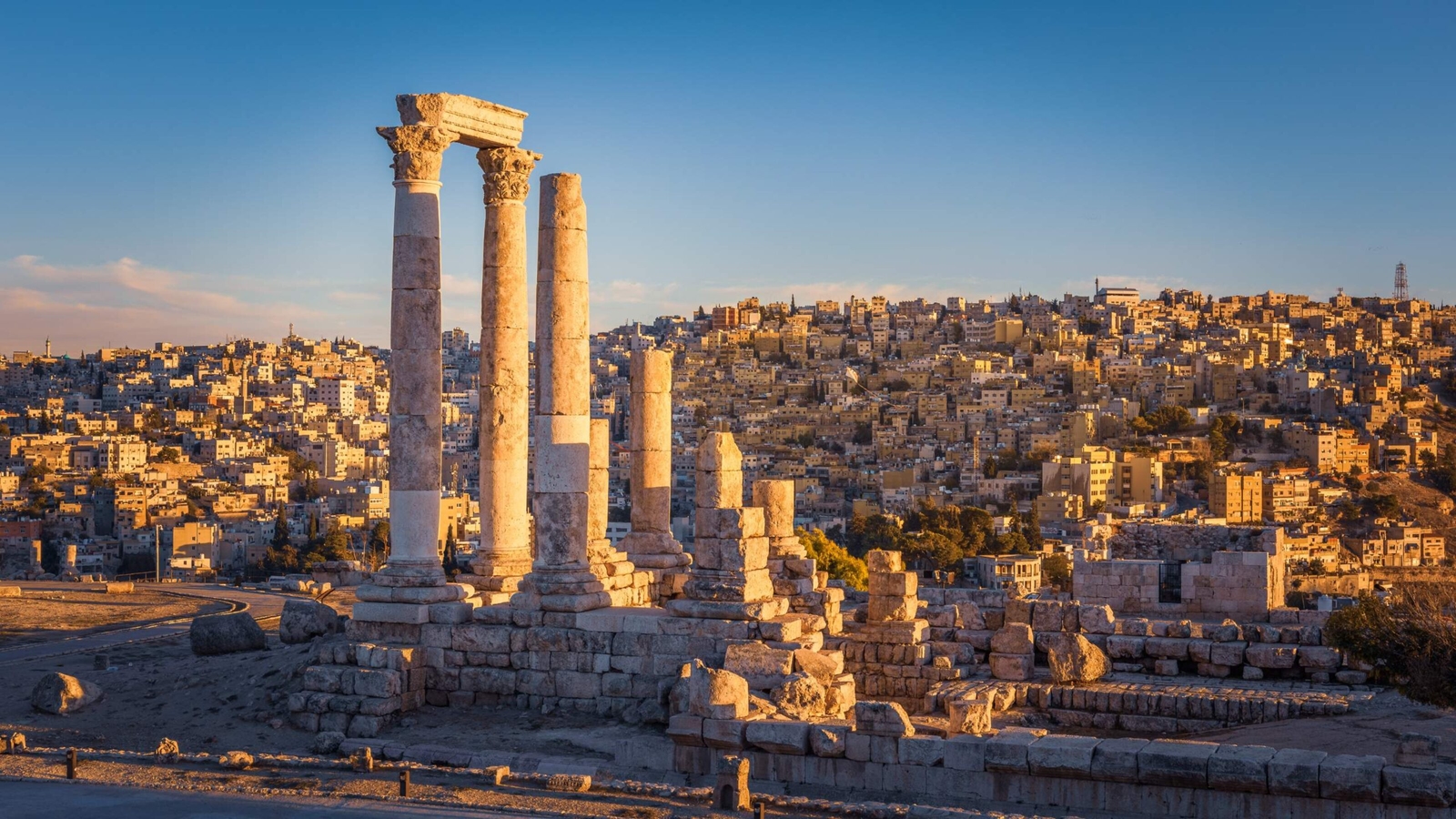 Ancient Roman columns of the Temple of Hercules overlook a hillside city in Amman, Jordan, during sunset.