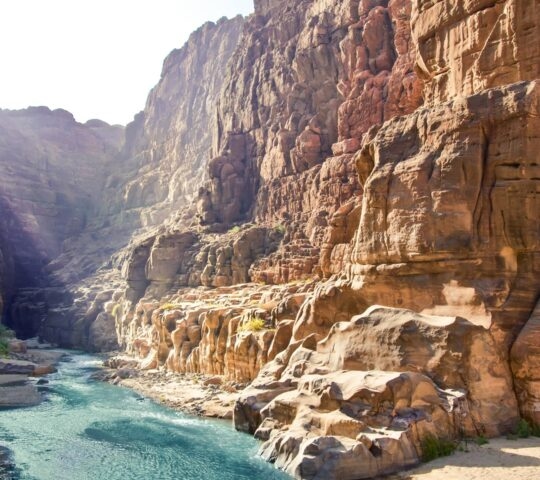 A bright blue river winds through a deep canyon with high, rugged rock walls.
