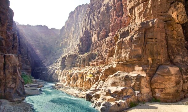 A bright blue river winds through a deep canyon with high, rugged rock walls.