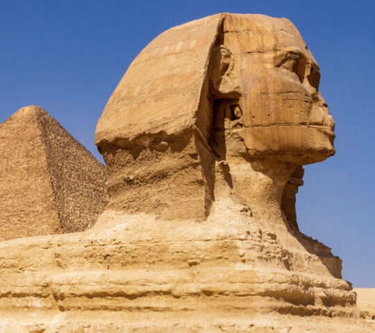 Sphinx carving in front of Egyptian pyramid with tourists below