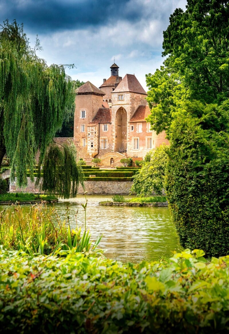 A beautiful historic chateau building in France, with a lake out front with willow trees around the edge