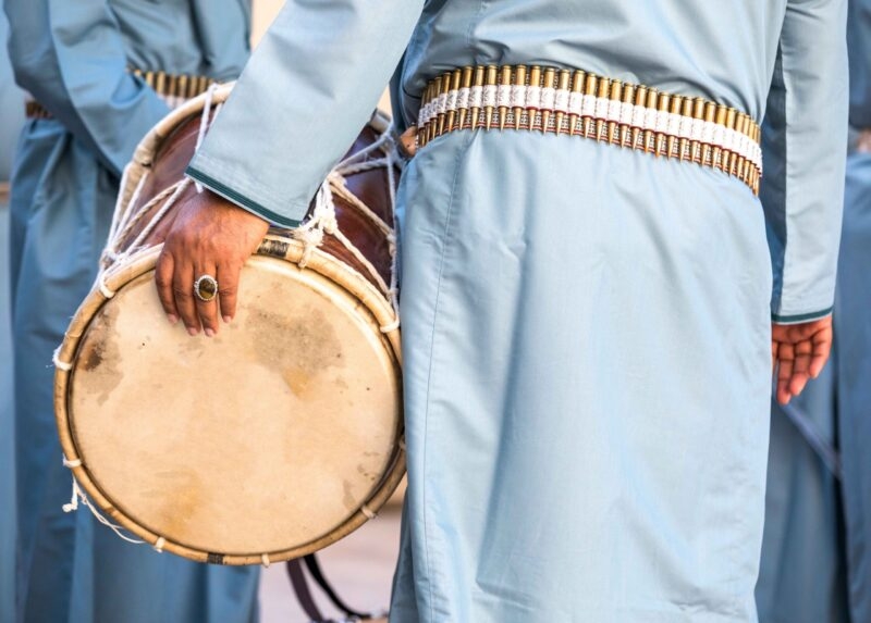 Close-up of a drummer in blue traditional dress with a bullet belt on luxury Oman tours.