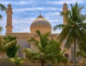A beautiful white mosque with golden domes seen through palm fronds on luxury Oman trips.
