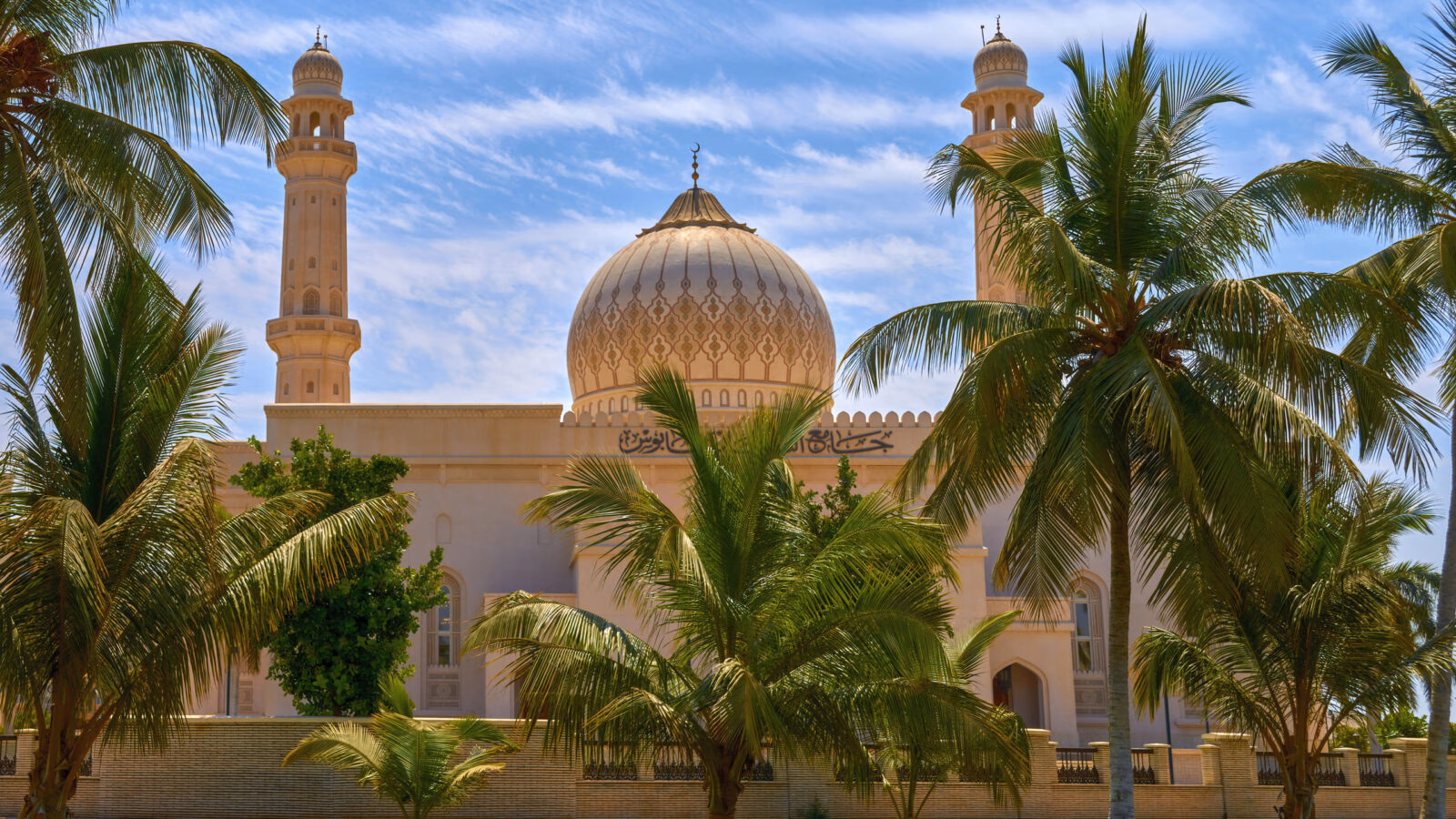 A beautiful white mosque with golden domes seen through palm fronds on luxury Oman trips.