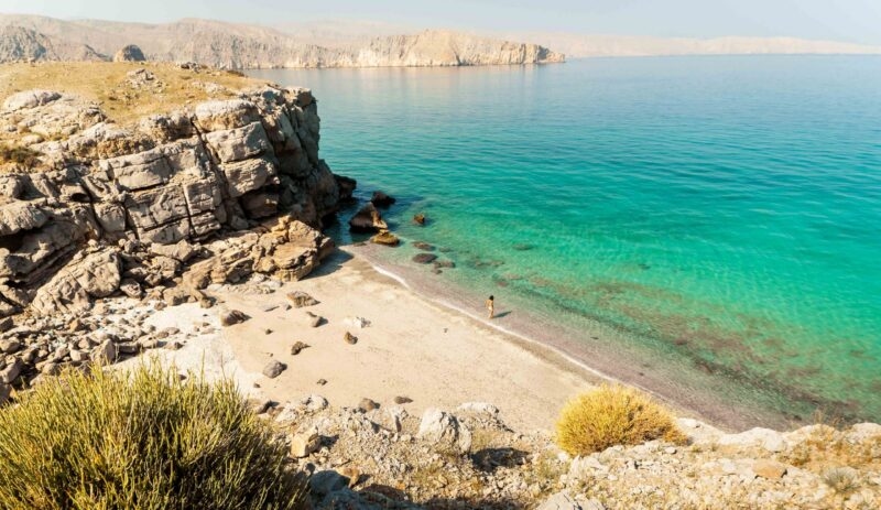 High angle view of a person on a pristine beach with turquoise water during luxury Oman tours.