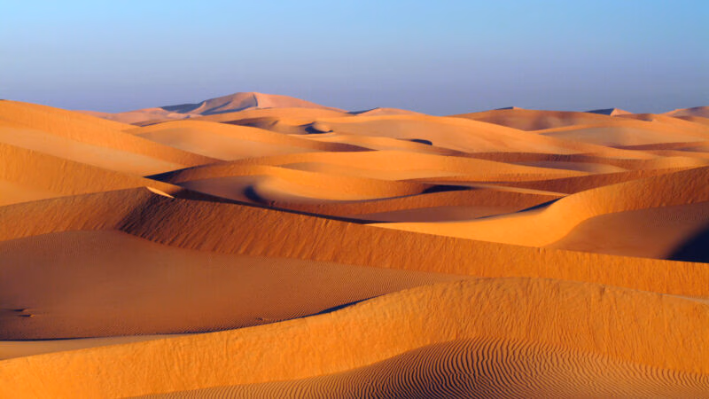 Sweeping orange sand dunes under a clear sky, typical of luxury Oman vacations.