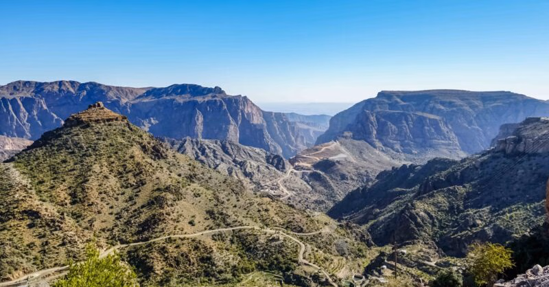 Wide landscape view of a mountain range and valley road on luxury Oman vacations.