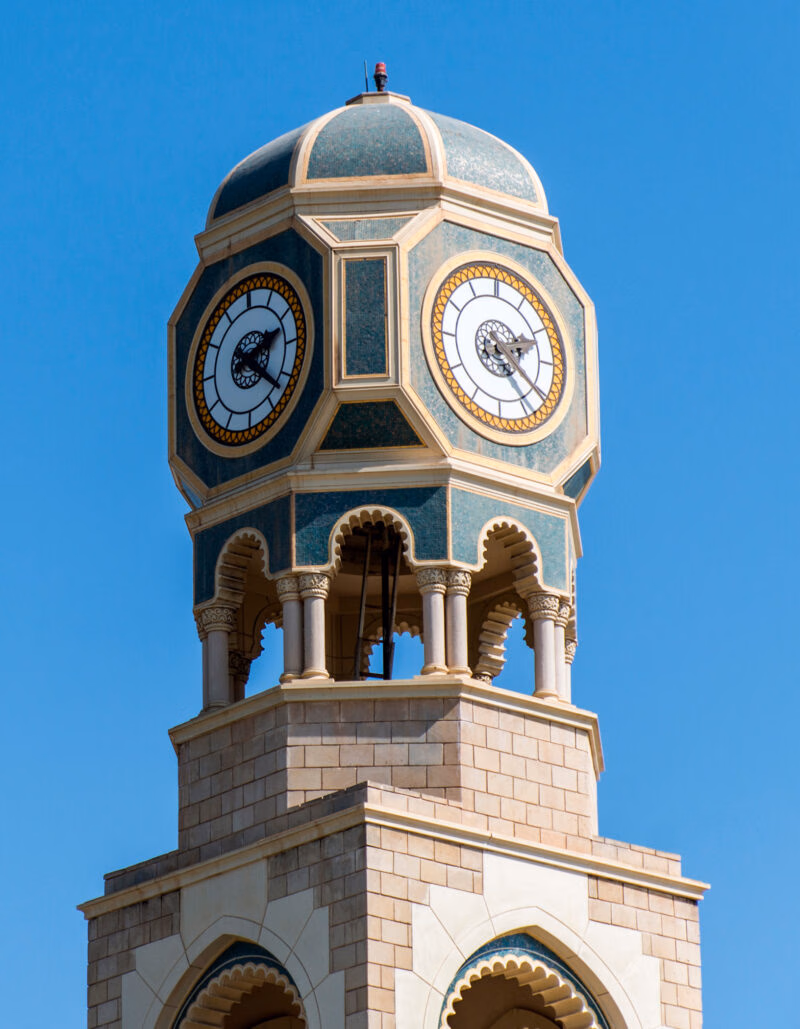 A decorative green and tan clock tower against a clear blue sky on luxury Oman holidays.