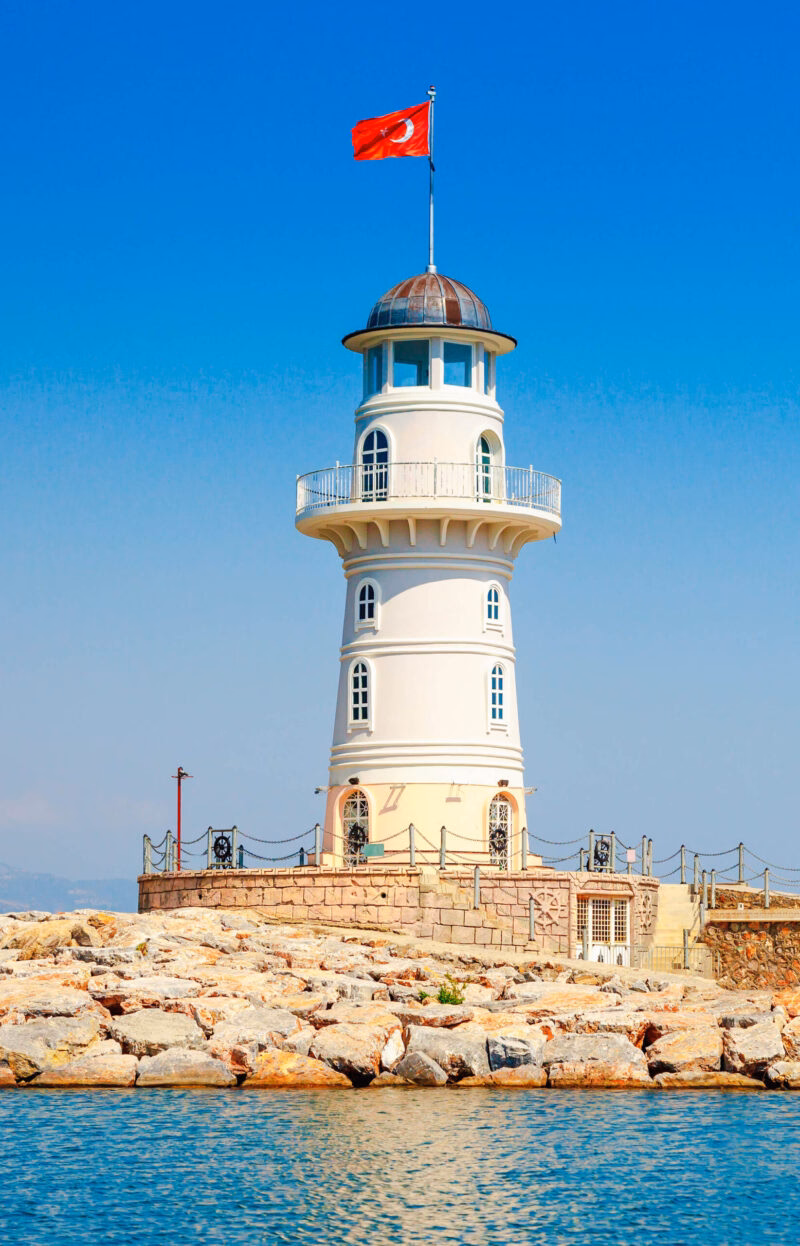 A white lighthouse with a red Turkish flag on top, viewed during luxury Turkey Asia holidays.