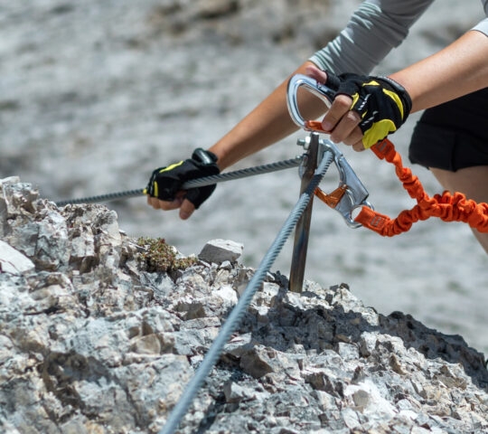Close-up of a climber's hands using safety equipment on a fixed-rope mountain climbing route.
