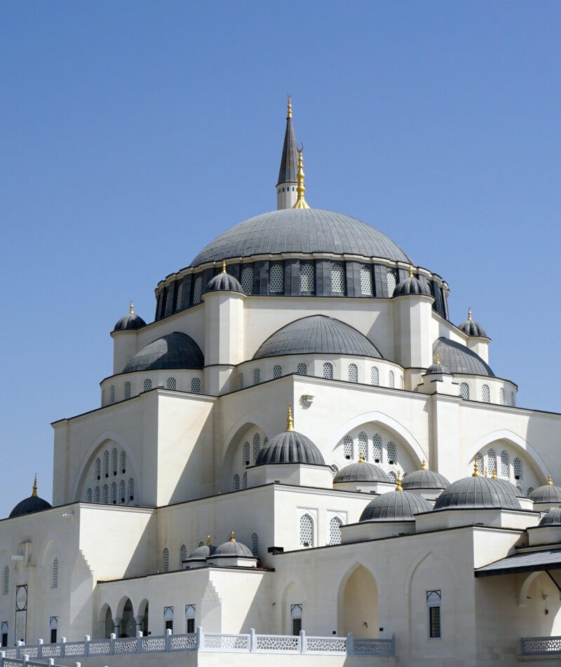 White domes and minaret of a large mosque under a blue sky during luxury United Arab Emirates holidays.
