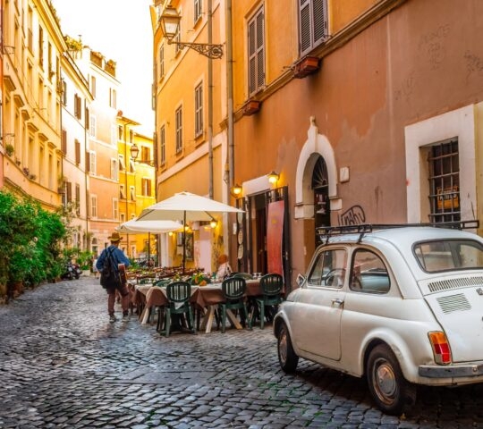 A Fiat 500 car parked along a colourful street in Rome, Italy.