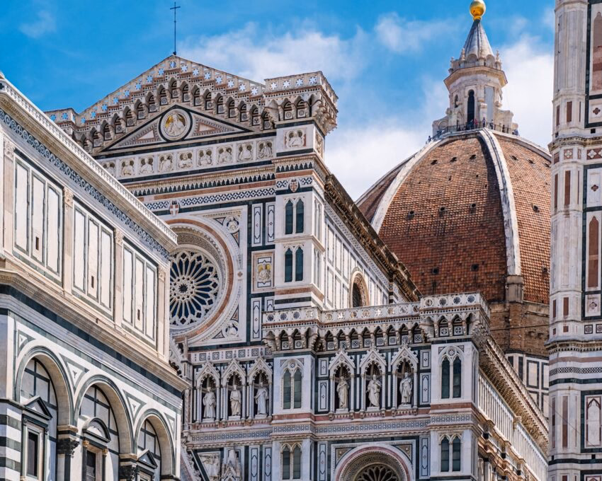 Close-up of the ornate white and green marble facade of a cathedral with a large brick dome in the background.