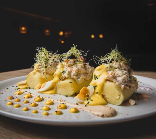 Three mounds of Peruvian Causa Rellena topped with creamy filling, huancaína sauce, sprouts, and sliced hard-boiled egg.