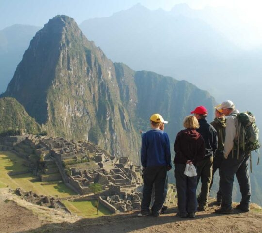 A group of five people wearing hiking gear stands on a high viewpoint overlooking the vast ruins of Machu Picchu and a massive mountain, ideal for luxury Machu Picchu trips.