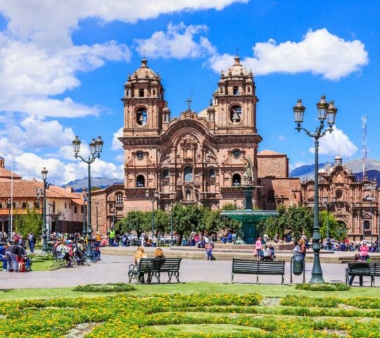 The large, ornate Church of La Compañía de Jesús in Cusco's main plaza, with people seated on benches in the foreground.