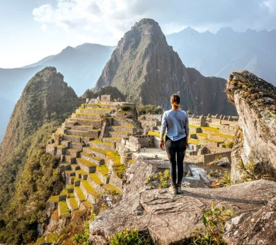 Traveller standing on a rock overlooking Machu Picchu, Peru
