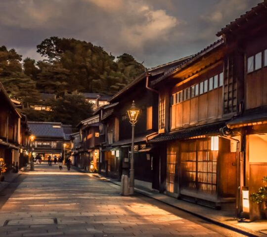 A quiet traditional Japanese street at dusk with glowing lanterns and wooden storefronts under a cloudy sky.