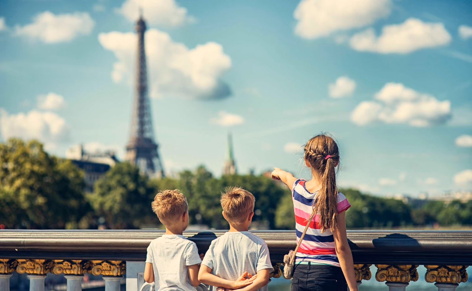 Three children looking at the Eiffel tower from a bridge over the Seine