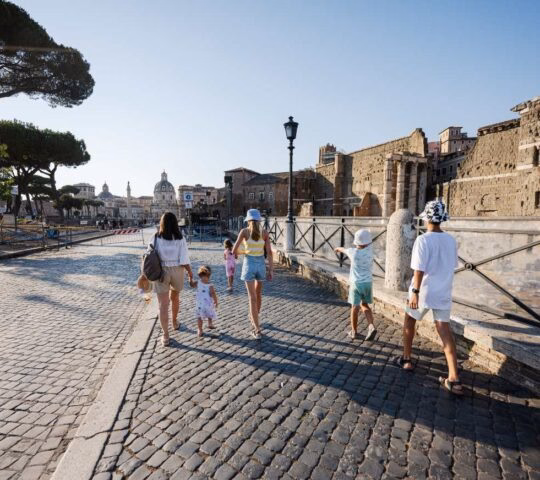 People walking on a cobblestone street in Rome near ancient stone ruins.