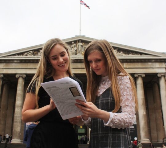 Two women looking at a paper document in front of the columns of the British Museum.