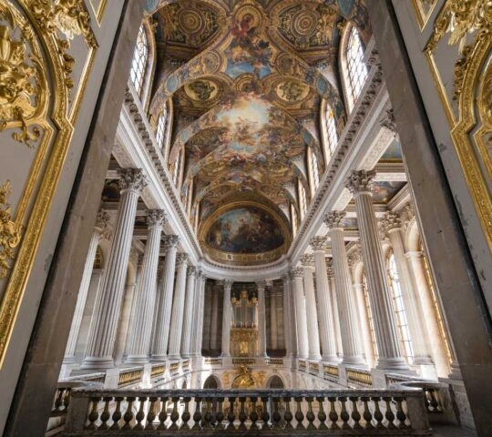 Grand baroque hall with gold carvings, white columns, and painted ceiling.