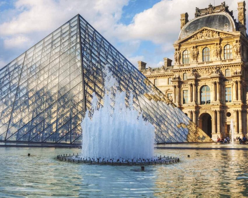 The glass Louvre Pyramid behind a splashing water fountain in Paris.