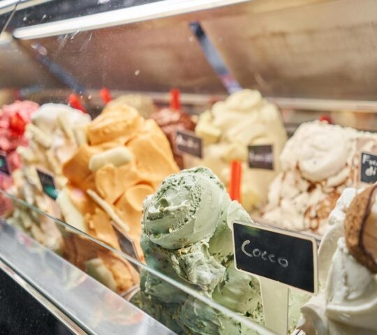 Various flavors of colorful Italian gelato are displayed in a glass case with a "Cocco" label visible.