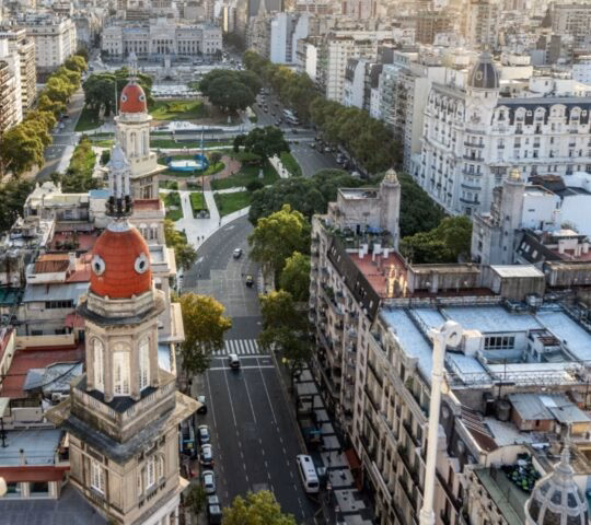 High-angle view of a city with a central domed palace and park during a bright orange sunset.