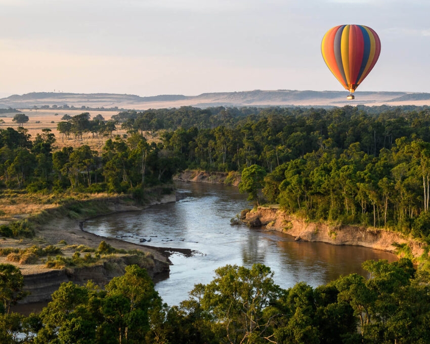 A rainbow striped hot a air balloon drifting over a river and forest