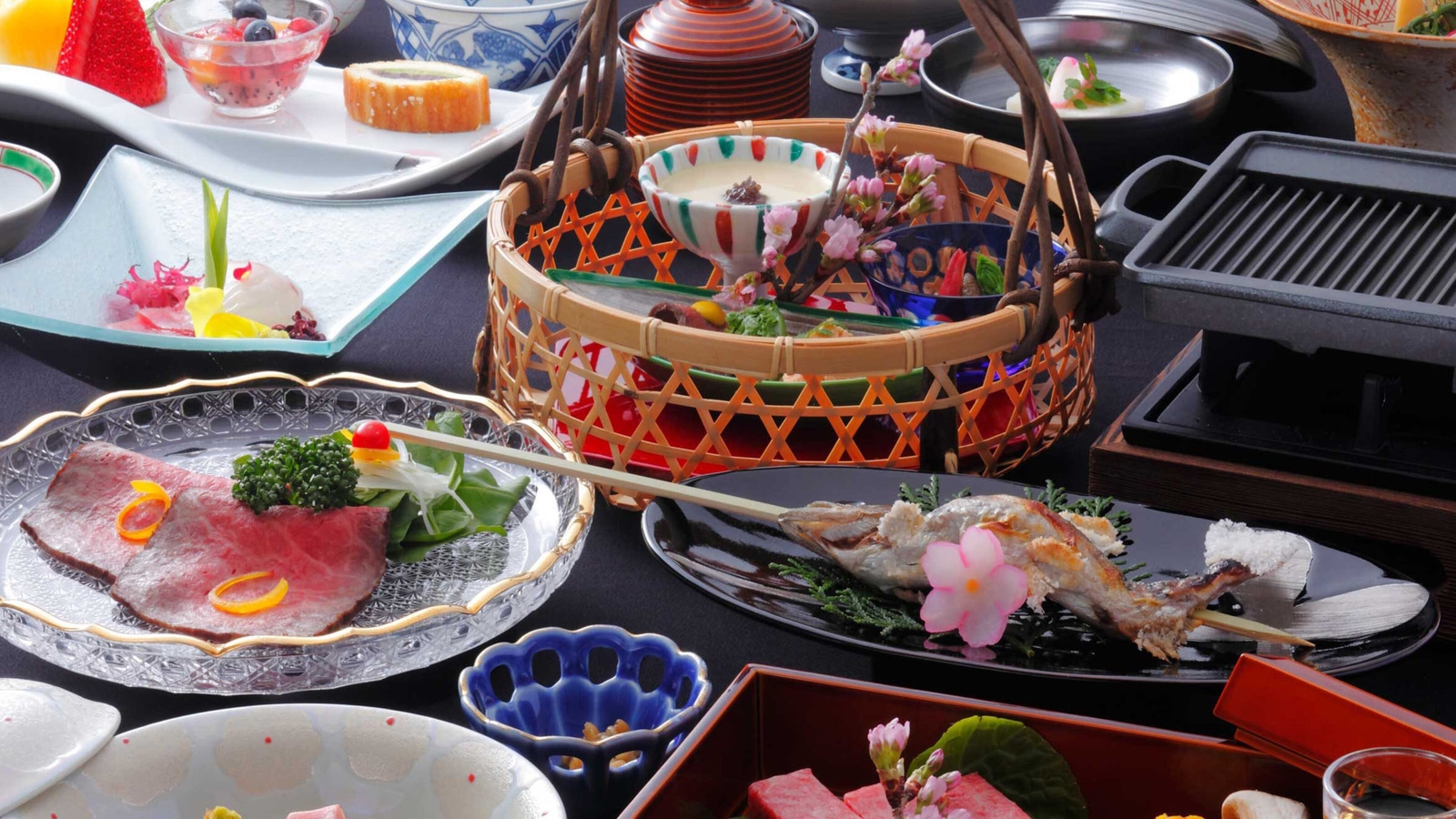 An assortment of traditional Japanese cuisine served in decorative bowls and baskets on a dark table.